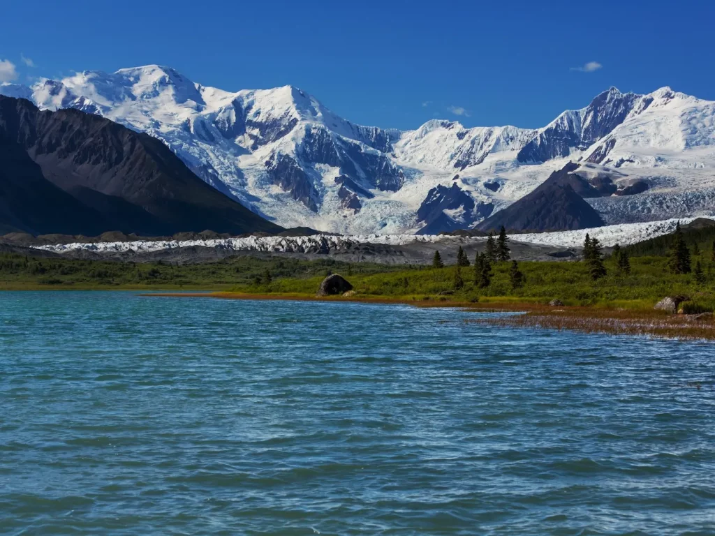 Schneebedeckte Berge und Gletscherlandschaft mit See im Vordergrund im Wrangell–St. Elias Nationalpark.