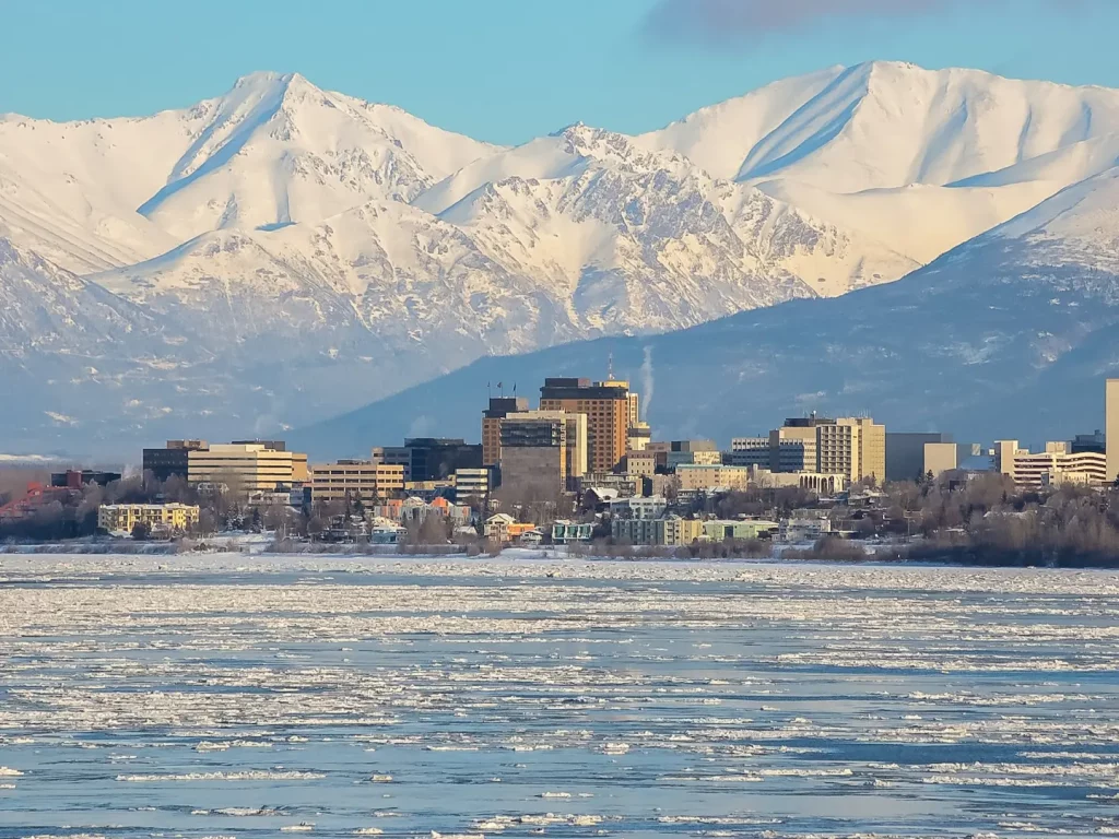 Stadtansicht von Fairbanks mit zugefrorenem Fluss und schneebedeckten Bergen im Hintergrund.