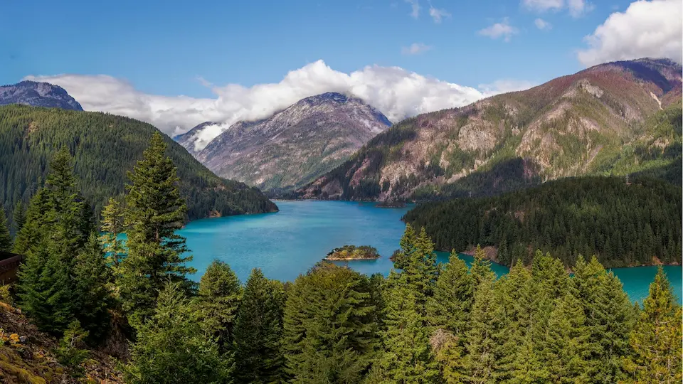 Türkisfarbener Bergsee umgeben von dichtem Nadelwald und hohen Bergen unter teilweise bewölktem Himmel