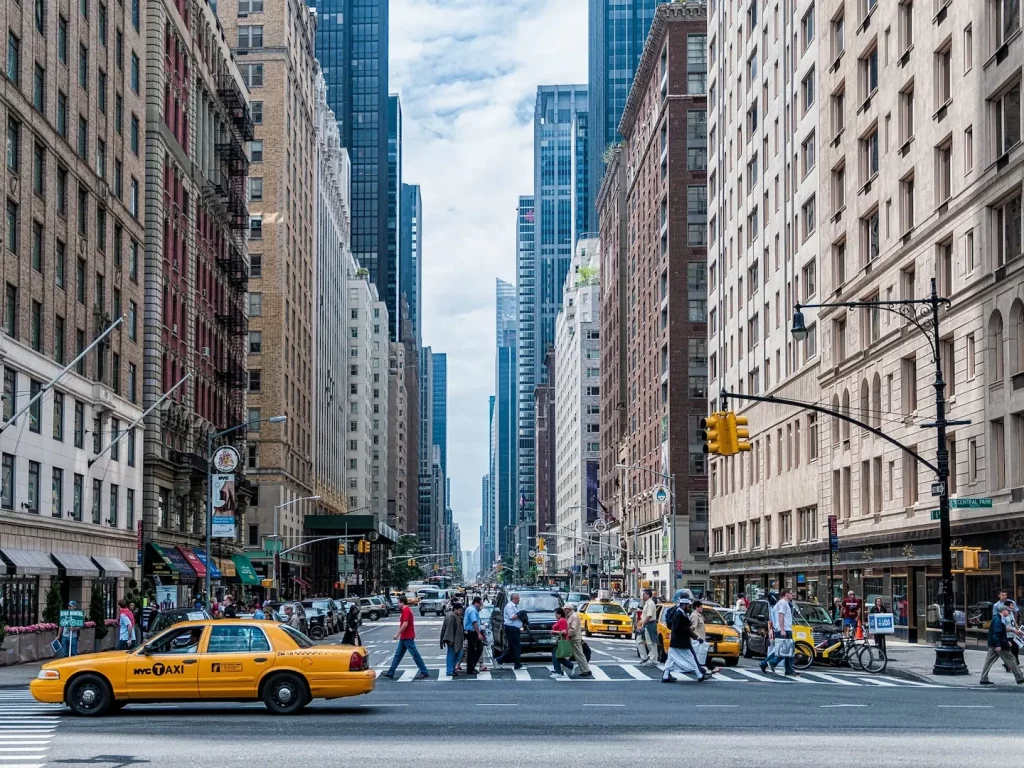Fußgänger überqueren eine Straße in New York City zwischen Hochhäusern und gelben Taxis.