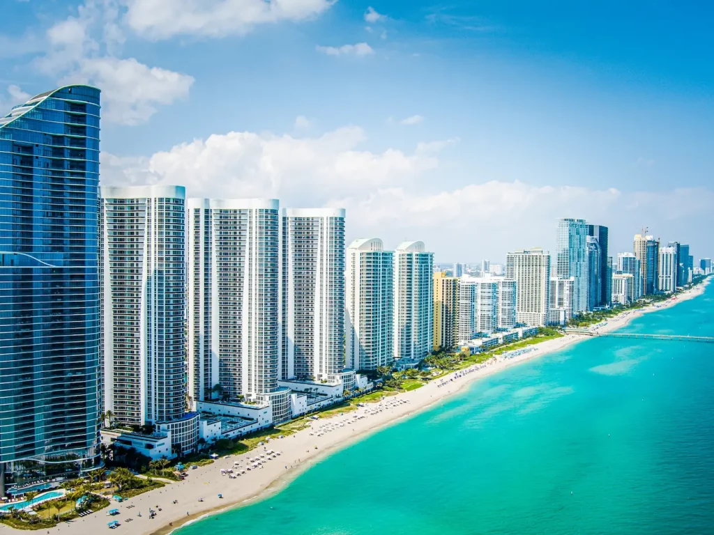 Hochhäuser entlang eines Sandstrandes mit türkisfarbenem Meer in Miami Beach.