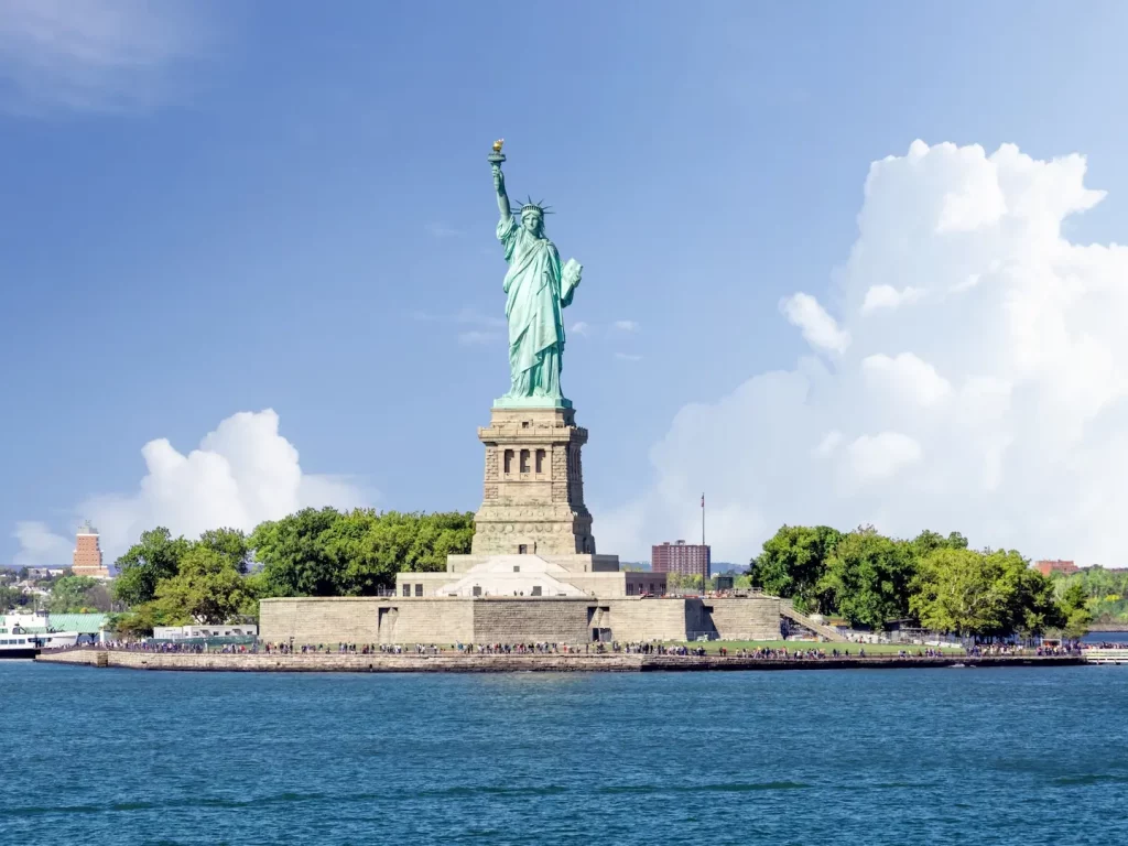 Freiheitsstatue auf Liberty Island mit erhobener Fackel vor blauem Himmel.