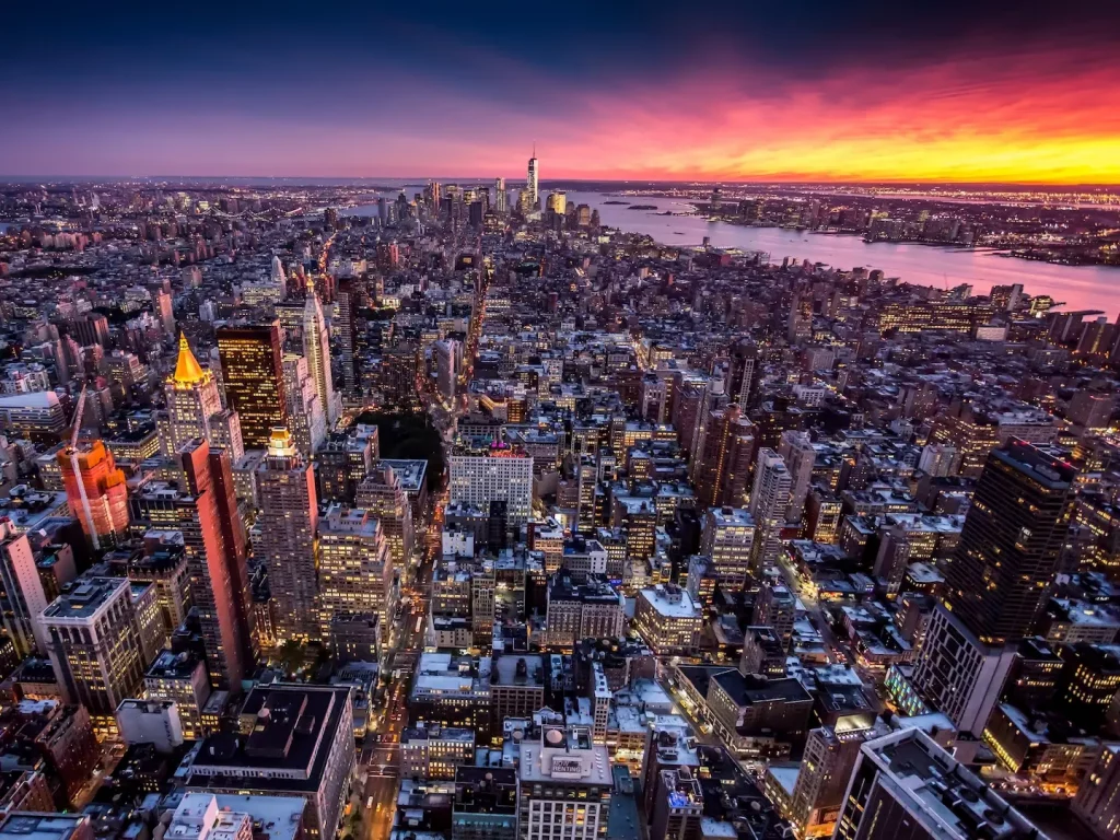 Luftaufnahme von Manhattan mit dicht bebauten Straßenzügen und leuchtendem Abendhimmel.