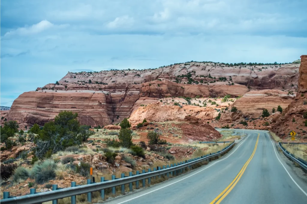 Zweispurige Straße führt durch eine weite Fels- und Wüstenlandschaft mit Sandsteinformationen