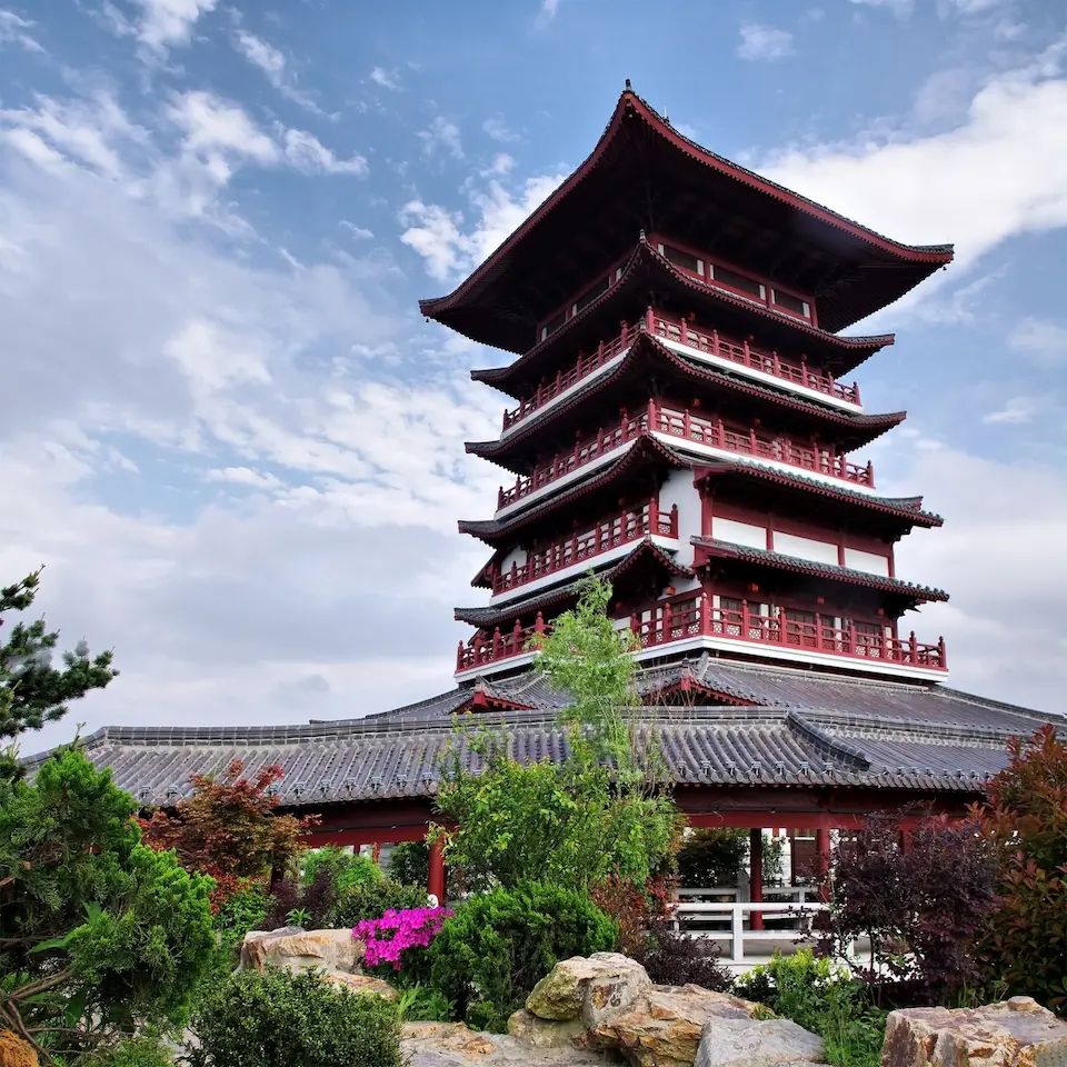 Mehrstöckige rote Pagode mit geschwungenem Dach, umgeben von Garten und Bäumen