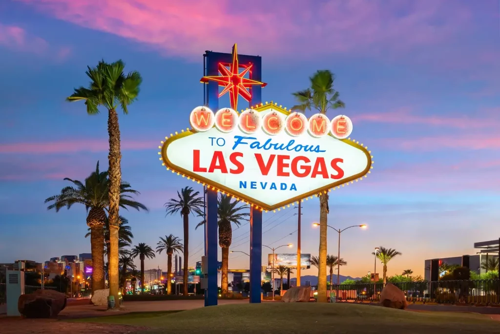 Beleuchtetes Welcome-to-Las-Vegas-Schild mit Palmen vor farbigem Abendhimmel